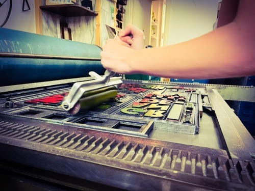 Workshop: mano che posiziona caratteri mobili di legno sul torchio tipografico